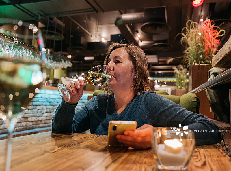 在自助餐厅喝葡萄酒、手持智能手机的女人肖像图片素材