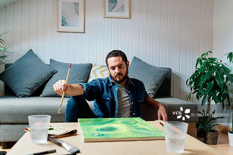 男人拿着刷子，一边绘画一边看着他的油漆图片素材