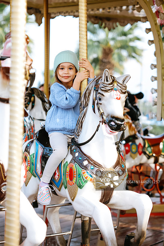 坐在旋转木马上的可爱孩子。可爱的女孩正在骑行游乐设施，庆祝欢乐图片素材