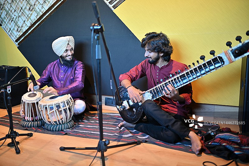 年轻的锡克教男人与另一位演奏西塔琴的年轻男人一起演奏塔布拉鼓图片素材