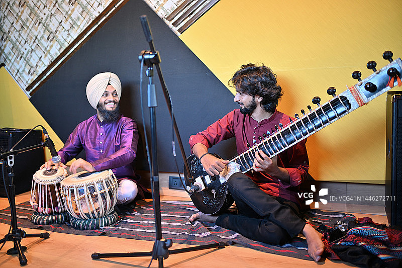 年轻的锡克教男人与另一位演奏西塔琴的年轻男人一起演奏塔布拉鼓图片素材