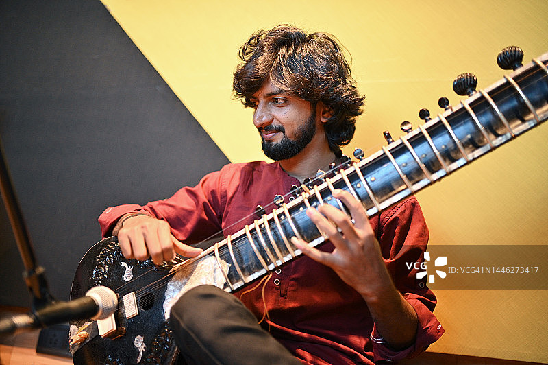 年轻男人享受弹奏西塔琴图片素材