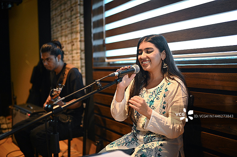 年轻女子演唱印度古典歌曲，贝斯吉他手演奏西方音乐，创造融合图片素材