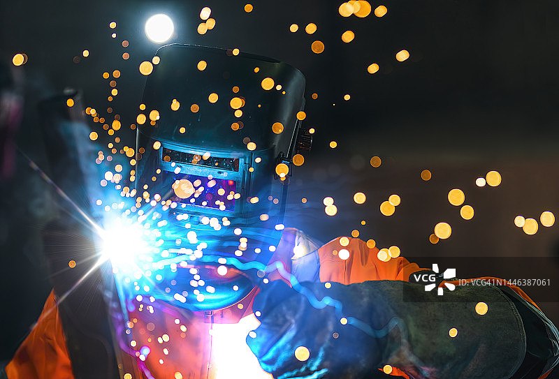 焊接工人穿戴工业制服和焊接面罩在工厂车间工作图片素材