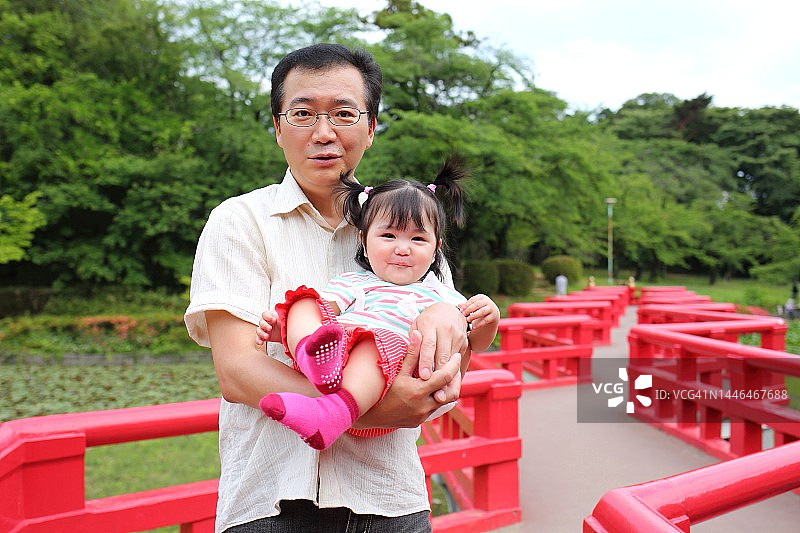 父亲抱着孩子站在日本红色桥梁上，留有复制空间。岩槻城址公园桥图片素材
