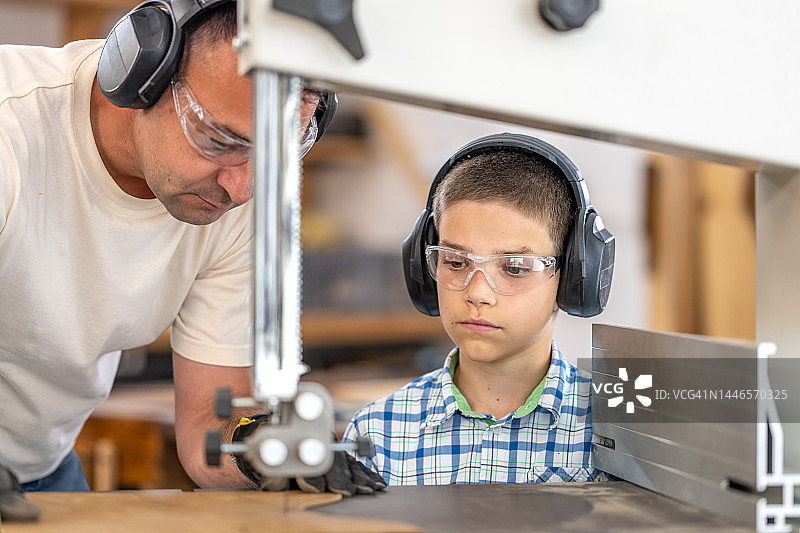 儿子观看父亲用电动曲线锯切割木板特写图片素材