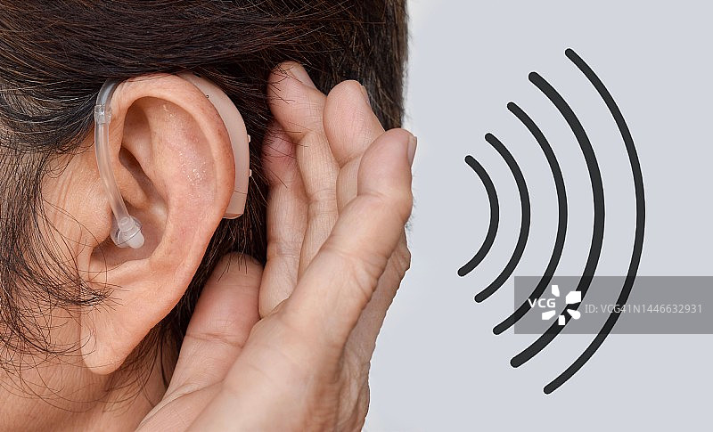 佩戴在耳聋亚洲女性耳朵里的电子助听器图片素材