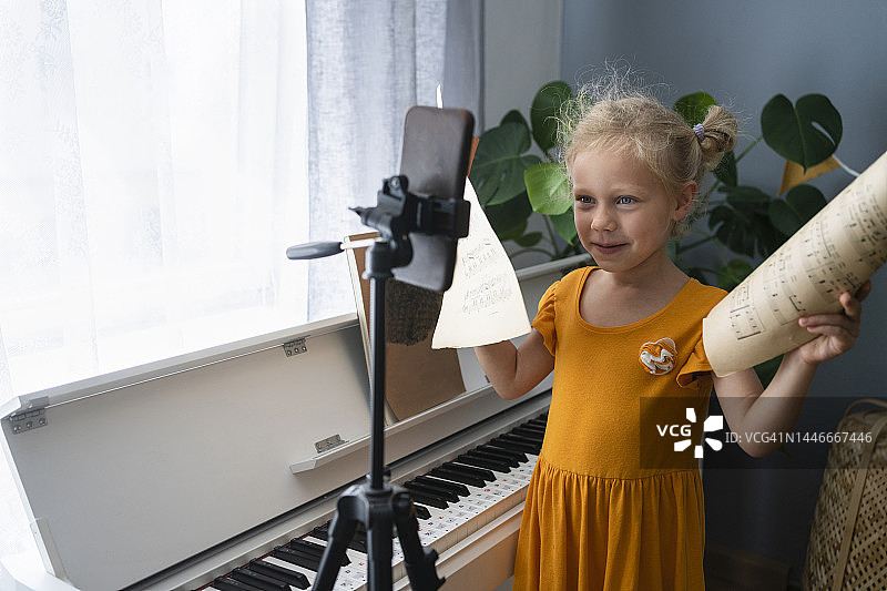 在家中，可爱女孩的三脚架上放着带有音符的智能手机图片素材