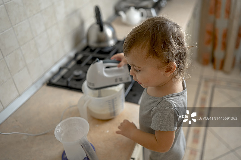 幼儿在家中厨房用电动搅拌器搅拌面糊图片素材