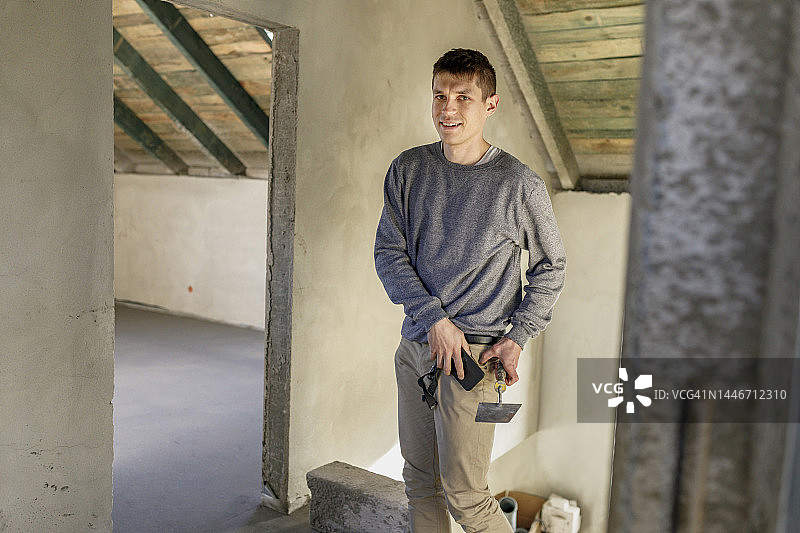 微笑的年轻男人在家拿着泥刀和智能手机图片素材