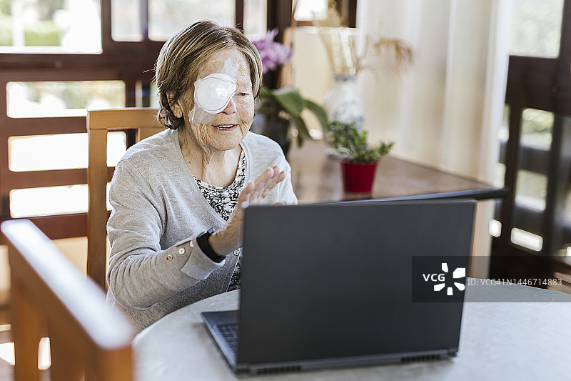 微笑的受伤老年妇女在视频通话中挥手图片素材