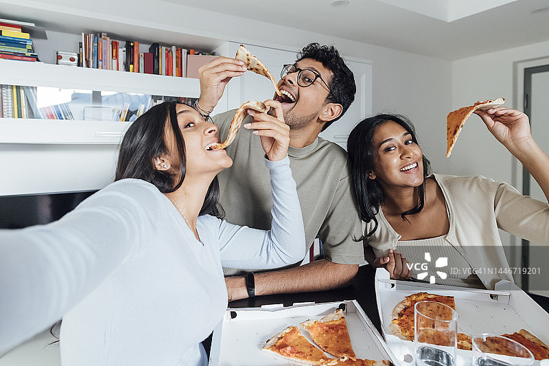 快乐的年轻女子与在家吃披萨的男人和女人自拍图片素材