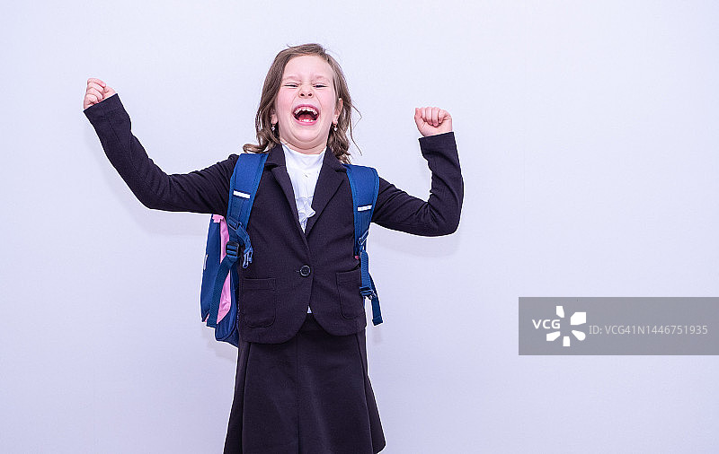 快乐的白人女学生，7岁，身穿黑色西装，背着书包，看着镜头挥手图片素材