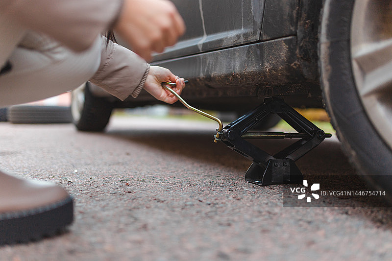 年轻女子用千斤顶抬起汽车的特写图片素材