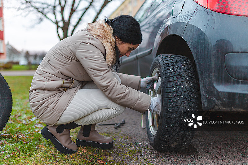 年轻女子在她的车上更换冬季轮胎。图片素材