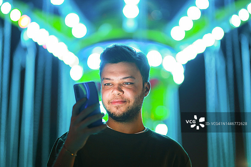 年轻男人用手机玩游戏，背景是彩色散景灯光图片素材