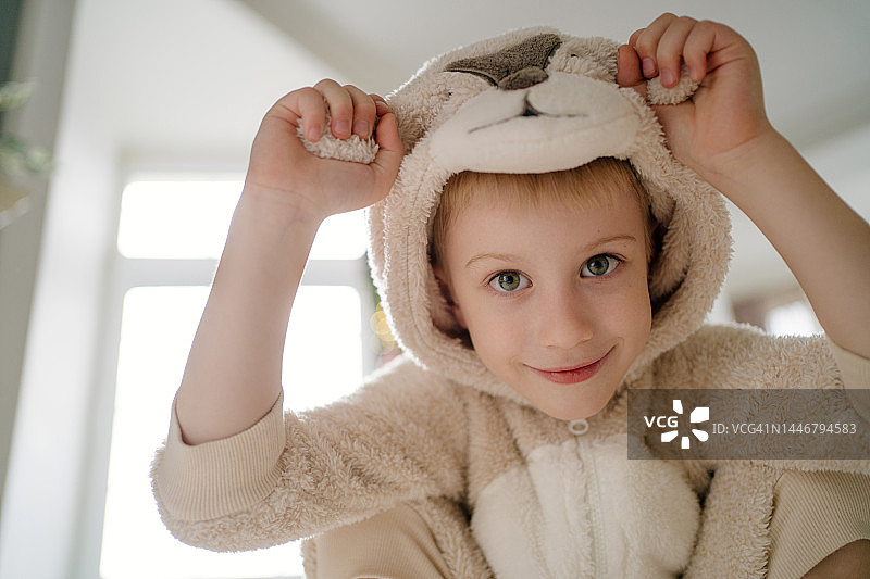 嬉戏的微笑男孩，双手拿着熊服装帽子的耳朵，看着镜头大笑图片素材
