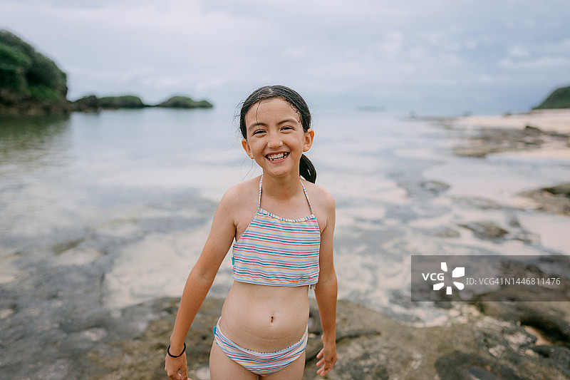 快乐的8岁女孩在黄昏时分的海滩上对着镜头大笑图片素材