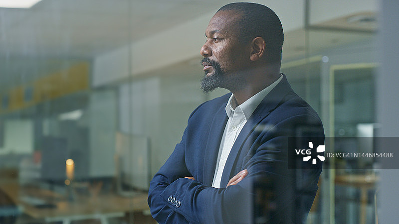 商界黑人交叉双臂思考，在公司工作，为公司展望。办公室商人，员工的想法和非洲工人在西装由窗口为职业生涯图片素材
