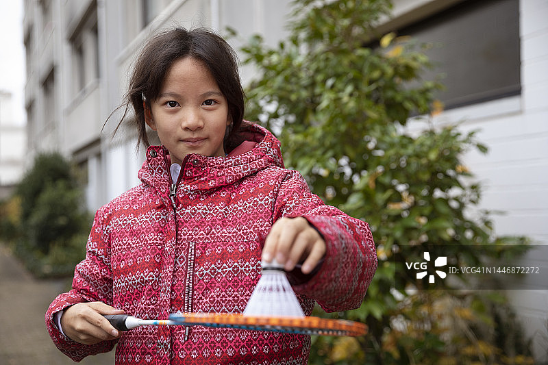 秋日里在公寓楼外穿着红粉色保暖外套，用羽毛球拍平衡羽毛球的女孩（9-10岁）图片素材