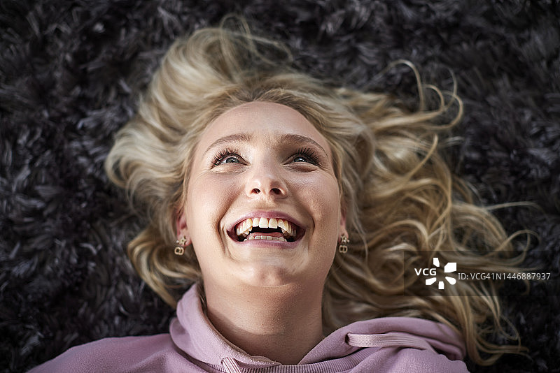 快乐的年轻女人躺在地毯上抬头看图片素材