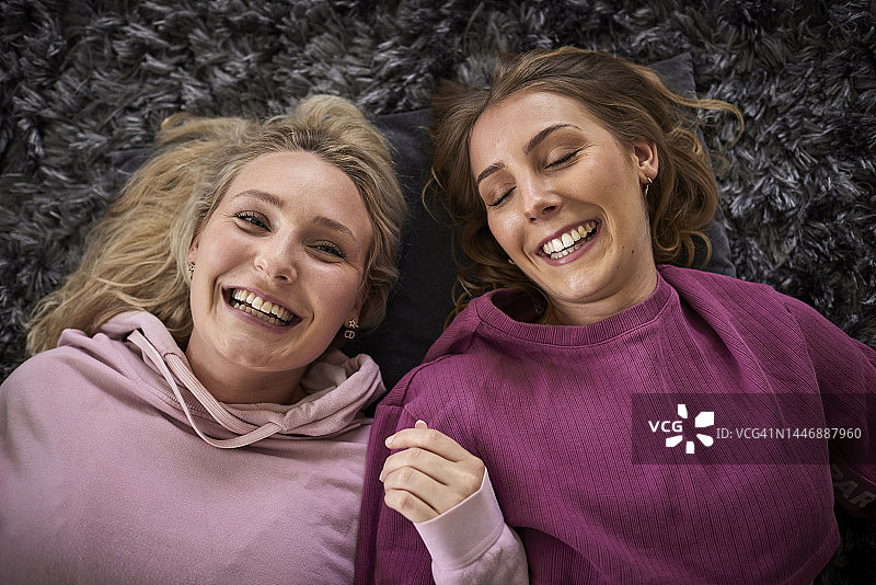 两名快乐的女性朋友一起躺在地毯上图片素材
