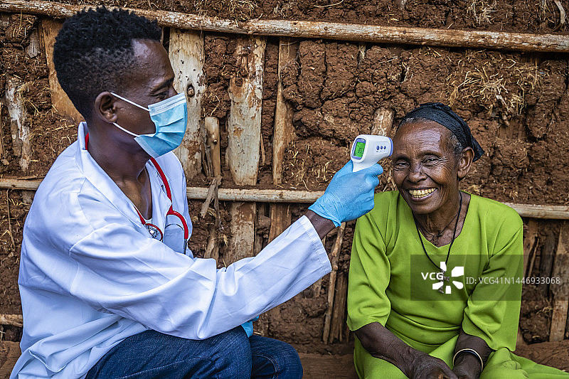 在东非偏远乡村，男医生为年长妇女测量体温图片素材