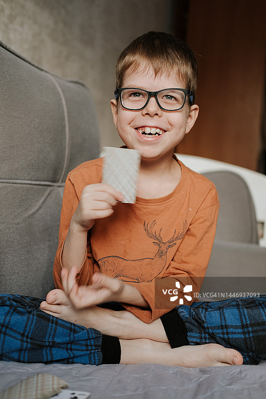 穿着睡衣的男孩坐在家里的沙发上玩牌图片素材