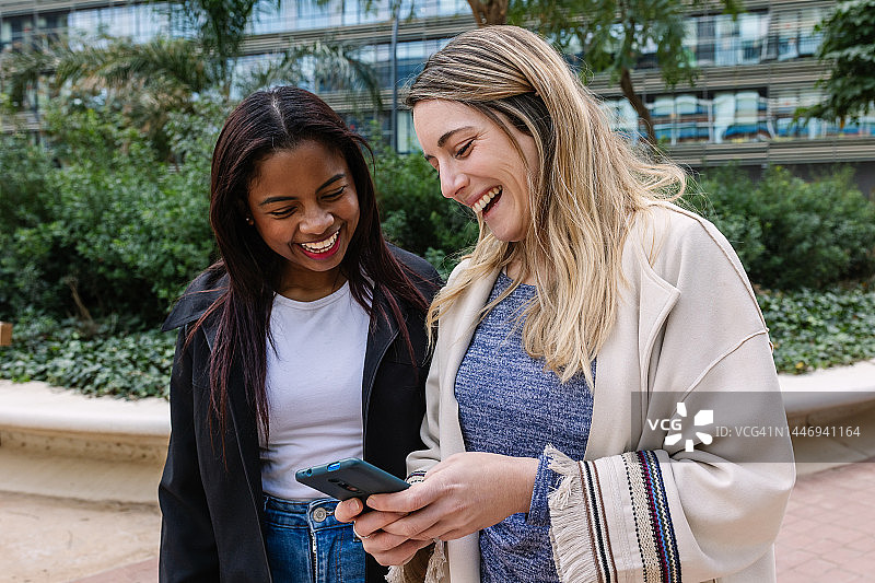 年轻的多种族女性朋友在户外使用智能手机玩耍。图片素材