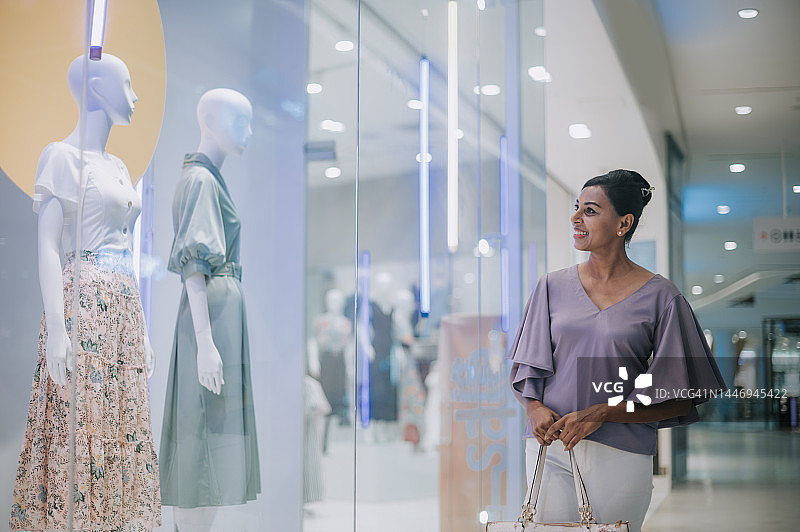 亚裔印度女子在购物中心橱窗购物，观看女装图片素材