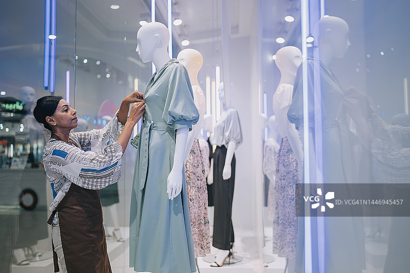 印度裔女店员在服装店橱窗里整理人体模型图片素材