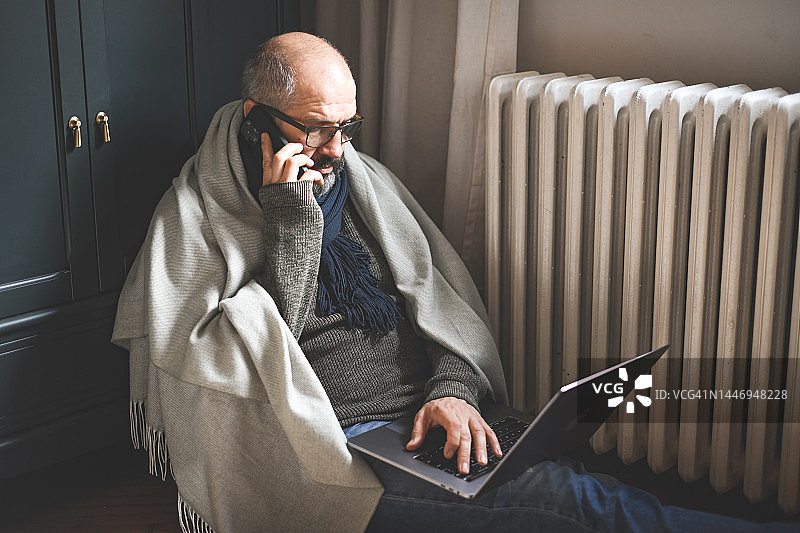 在家工作的成熟男人（暖气片、笔记本电脑、财务账单）图片素材