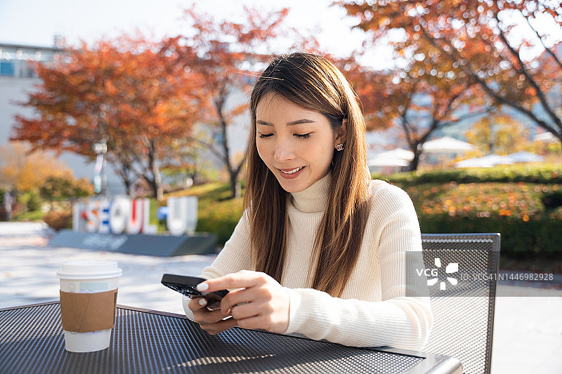 亚洲女人早上在首尔公园里坐着使用智能手机图片素材