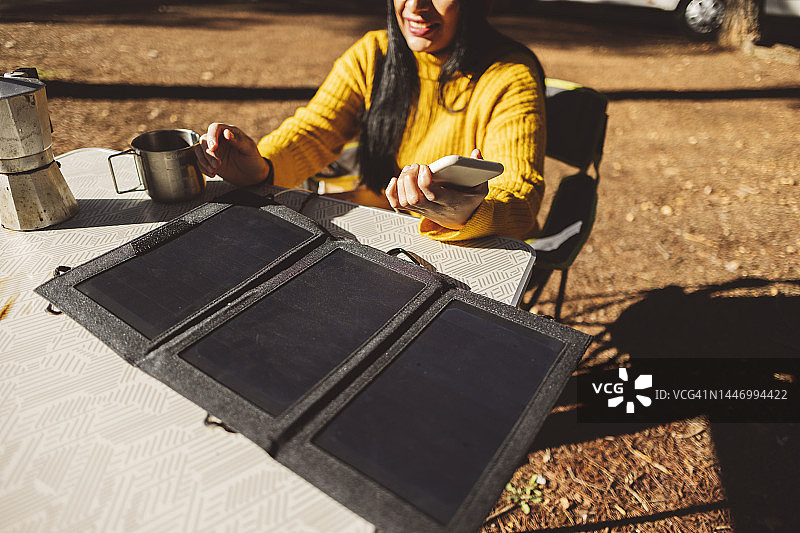 在户外使用太阳能电池板为手机充电的西班牙裔妇女图片素材