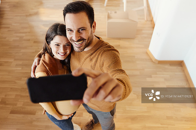 幸福的怀孕夫妇在新公寓自拍图片素材