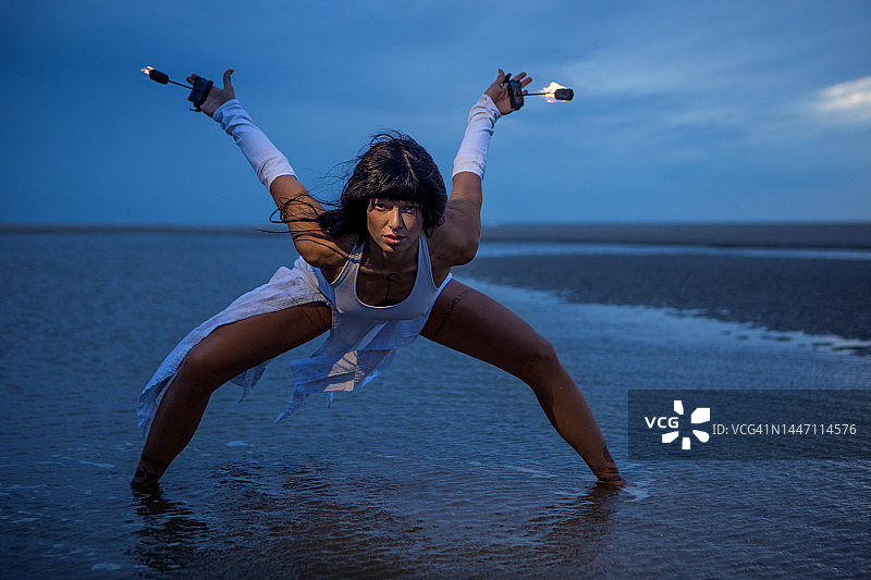 美丽的棕发女火舞者在黄昏时分的沙滩上表演。图片素材