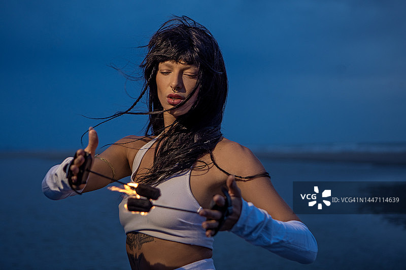 美丽的棕发女火舞者在黄昏时分的沙滩上表演。图片素材