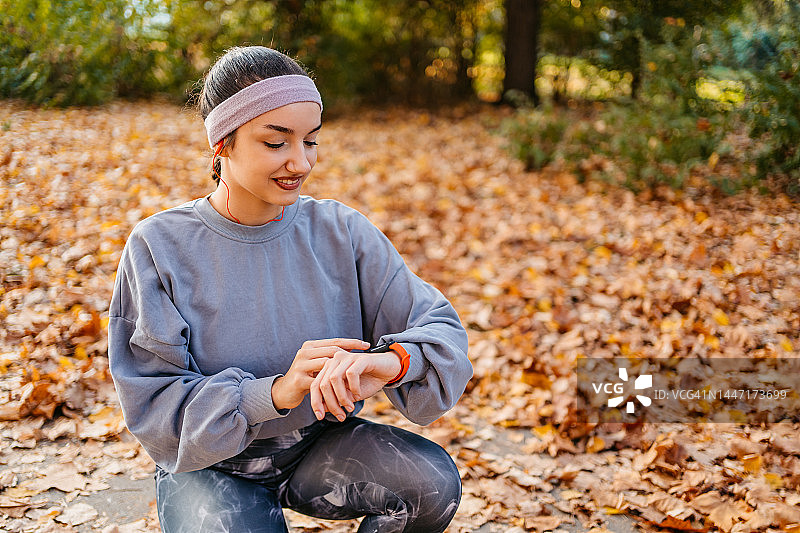 年轻女子在公园慢跑后，在智能手表上查看健身活动图片素材