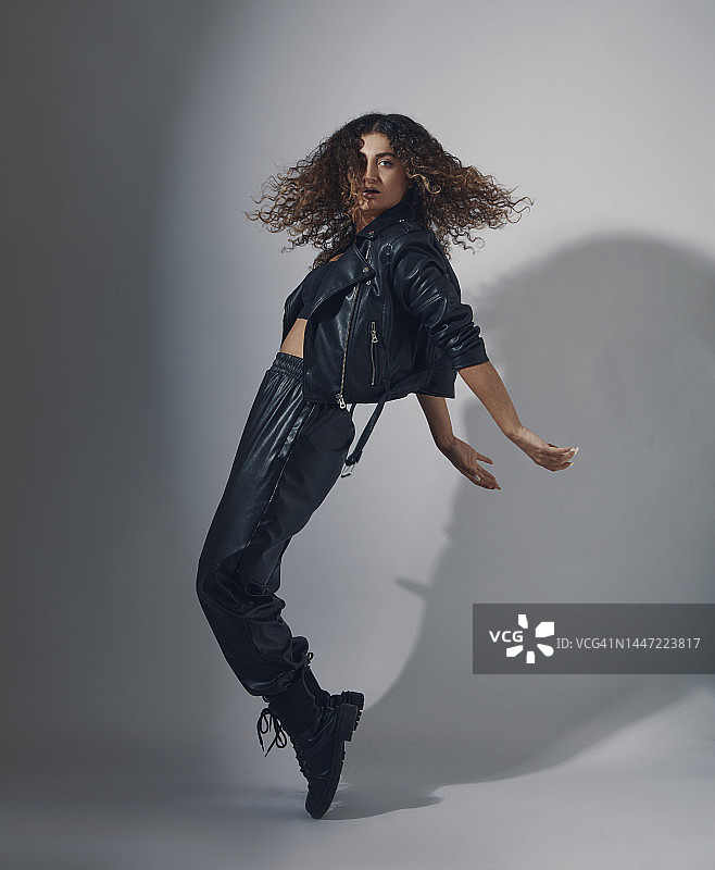 身穿皮夹克和皮裤、踮起脚尖站立的卷发时尚女模特图片素材