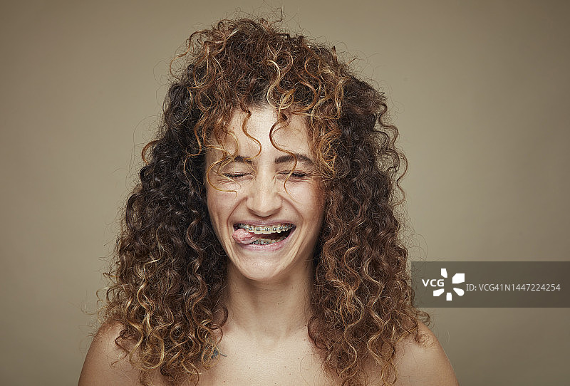 眨眼并伸出舌头的卷发年轻女人肖像图片素材