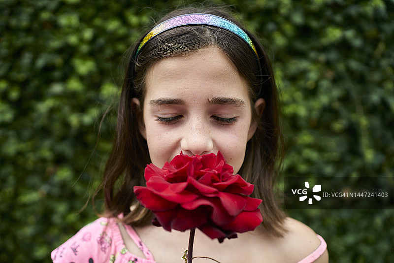 棕色头发的白人女孩闭着眼睛拿着红玫瑰闻着图片素材