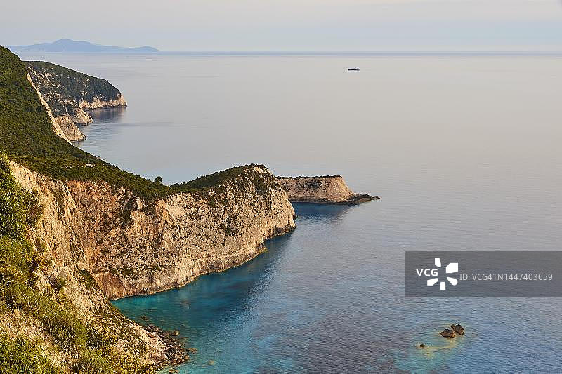 西南部孤独的海岸线，蓝色朦胧的天空，陡峭的岩石海岸，绿松石色的海洋，希腊莱夫卡达岛图片素材