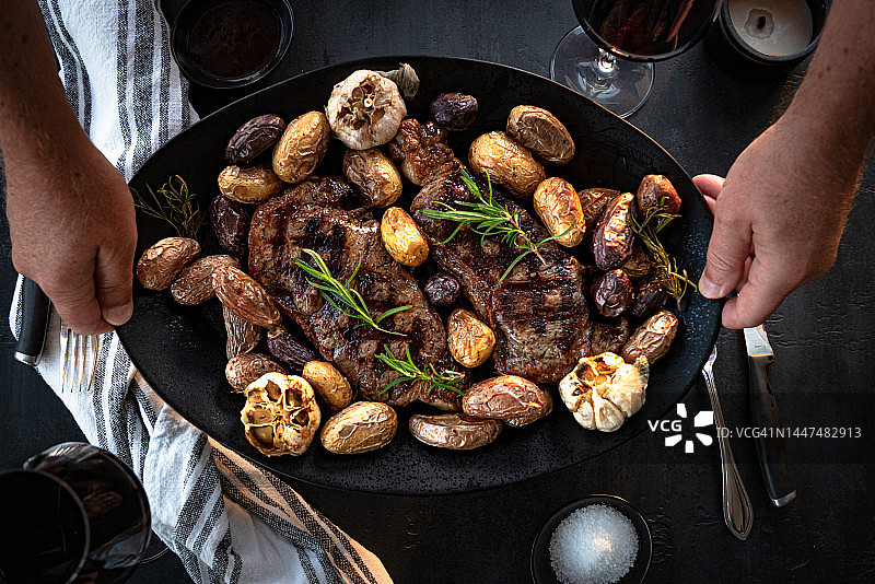 盘子里有2块烤牛排、土豆和大蒜的扁平风格照片图片素材