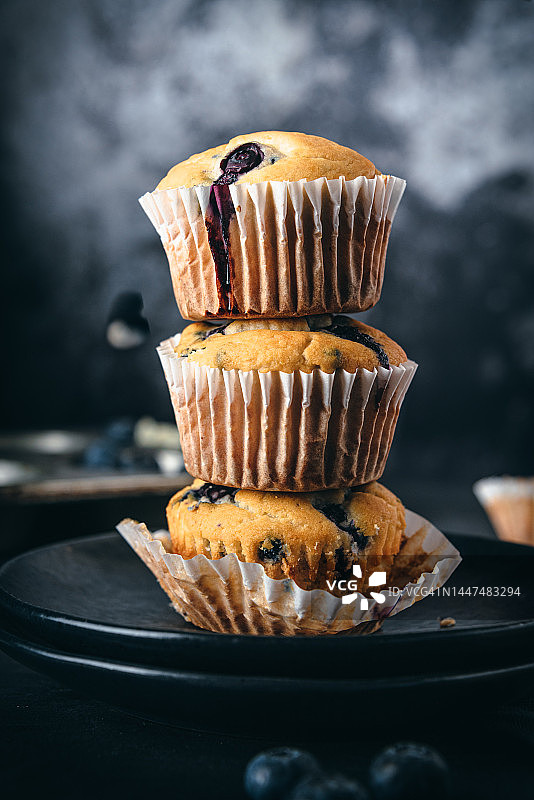 纸杯中堆叠的自制蓝莓松饼，周围环绕着新鲜蓝莓图片素材