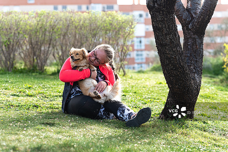 一位戴眼镜的金发女孩和她的狗坐在草坪上的肖像图片素材