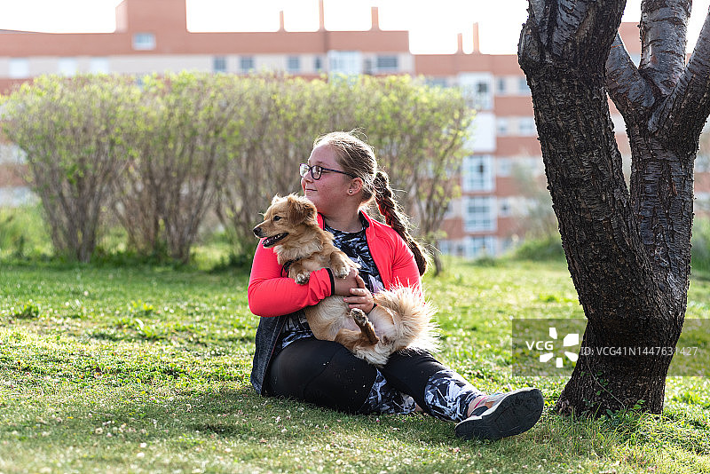 一位戴眼镜的金发女孩和她的狗坐在草坪上的肖像图片素材