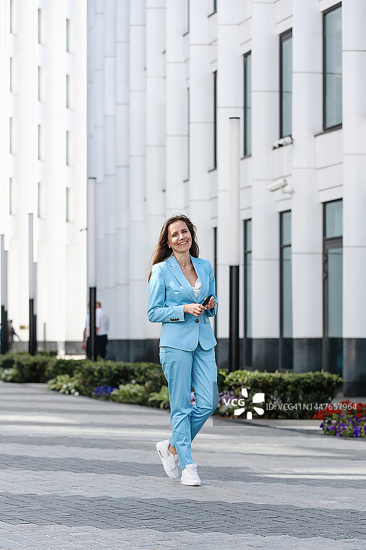 自信的年轻女商人行走在现代办公楼前图片素材
