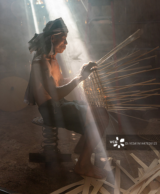 亚洲乡村生活方式：当地成年男性竹编工匠在茅草屋内制作竹篮和帽子图片素材