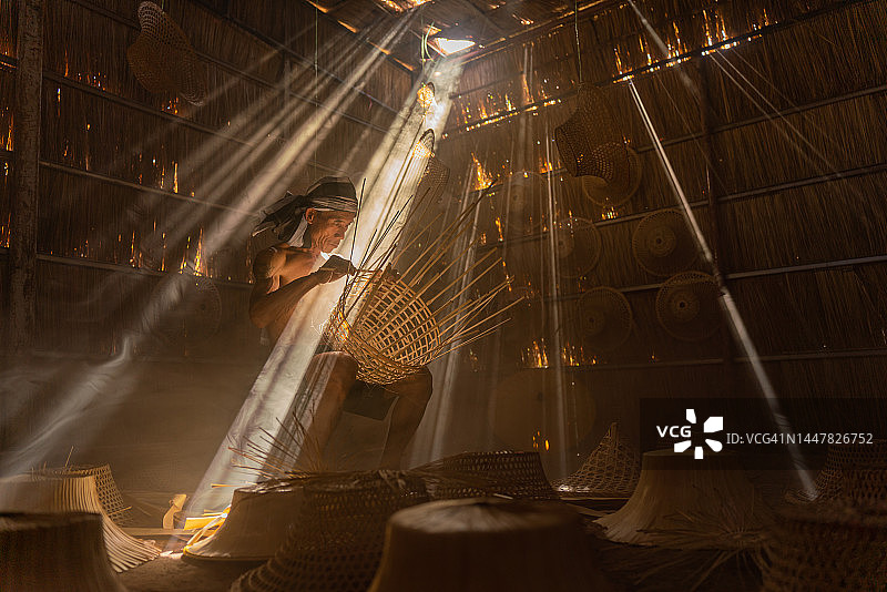 亚洲乡村生活方式：当地成年男性竹编工匠在茅草屋内制作竹篮和帽子图片素材