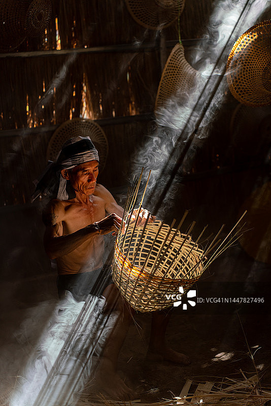 亚洲乡村生活方式：当地成年男性竹编工匠在茅草屋内制作竹篮和帽子图片素材